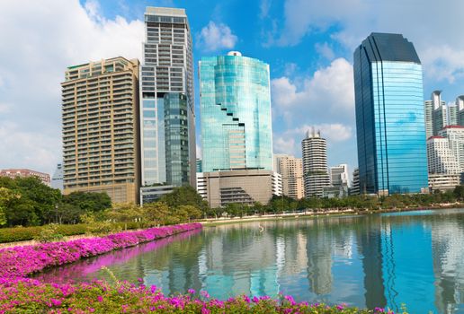 Modern city skyline of business district downtown and green park with lake and pink flowers in day under blue sky