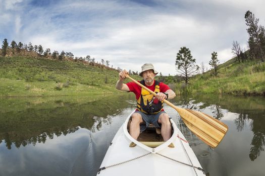 senior athletic paddler in a  decked expedition canoe on a lake with green vegetation - Horsetooth Reservoir, Fort Collins, Colorado