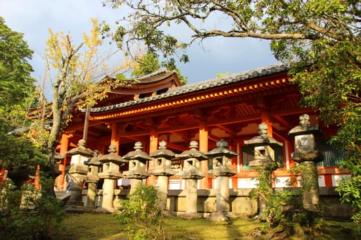 Line of concrete lanterns along the side of bright red wooden temple, Japan