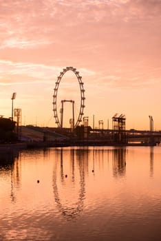 Silhouette of big ferris wheel in the pink sky with reflection in water