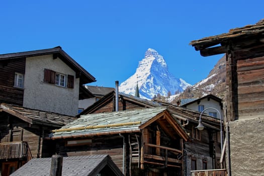 Old wooden lodges in Zermatt with a sun bathed Matterhorn behind.