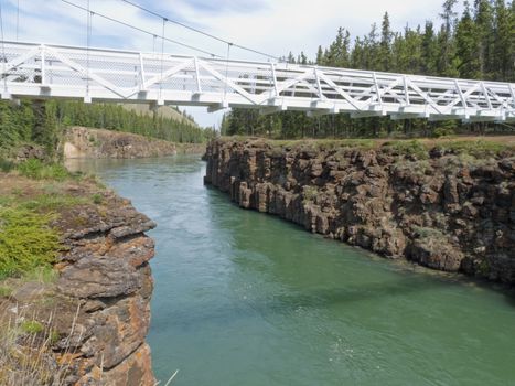 Miles Canyon Yukon River rock cliffs with white painted suspension swing bridge just south of the city of Whitehorse, Yukon Territory, Canada