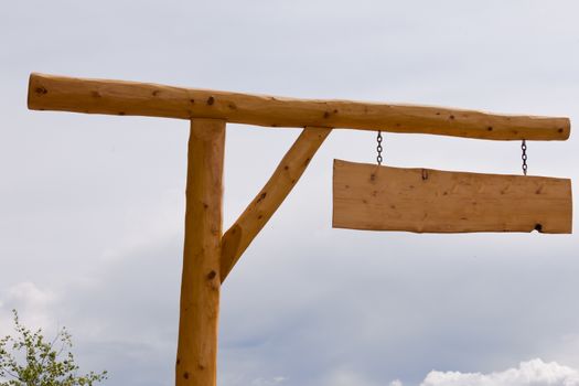 Blank rustic wooden sign with copyspace ready for your text message, hanging on pole with grey cloudy sky background