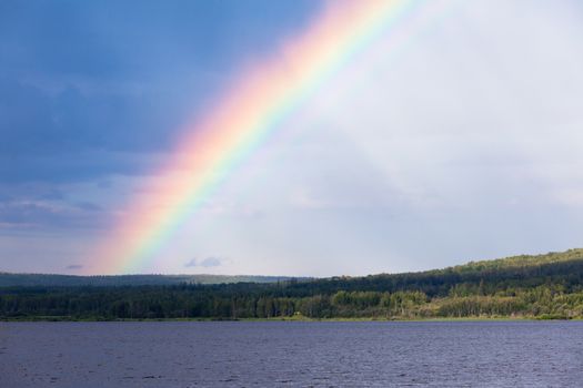 Intense Rainbow over surface of northern boreal forest taiga lake, northern British Columbia, Canada