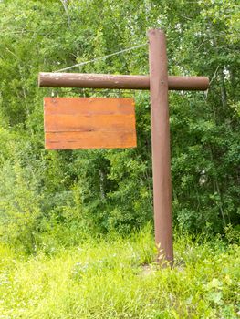 Blank rustic wooden sign with copyspace ready for your text message, hanging on pole with dense green forest background