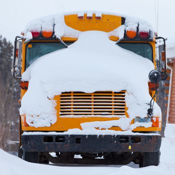 Snow covered front of parked school bus after heavy winter blizzard snow fall