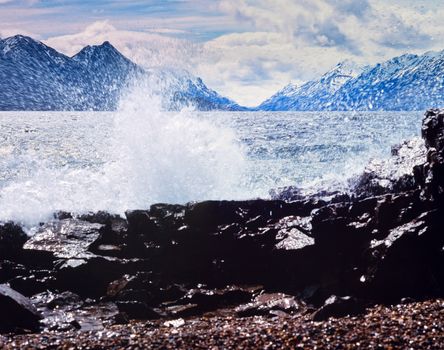 Strong wind and high waves on Lake Bennett rocky shore with distant high mountains on oposite lake side, Yukon Territory, Canada