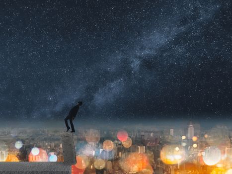 Concept of dangerous balance, business man dancing on a stone of the roof of city under stars in night.