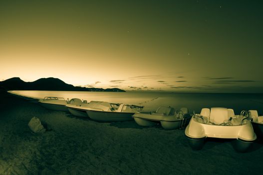 Pedal boats on the sea beach at night. Toned.