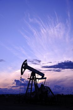 Oil and gas industry. Silhouette oil pump on a purple sunset sky background.