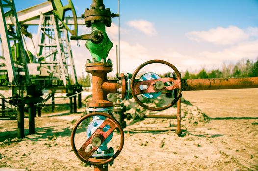 Wellhead with valve armature and pump jack. Extraction of oil. Toned.