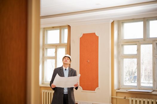 Engineer or architect in the white hard hat with the blueprint. Reconstruction interior.