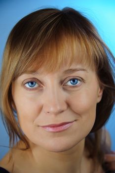 Portrait of adult woman with a smirk. Look at the camera. Blue background. Closeup.