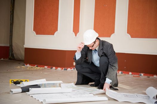 Architect or engineer in the white hard hat with the blueprint. Reconstruction interior.