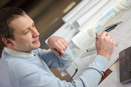 Engineer or architect in blue pullover is working on construction plans.