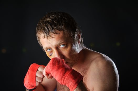 Portrait of a man with a bruise in a battle position. Clenched fists. Dark background.