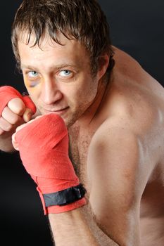 Portrait of a man with a bruise in a battle position. Clenched fists. Dark background.