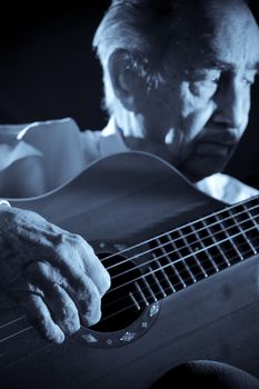 An elderly man in white shirt playing an acoustic guitar. Dark background. Monochrome.  Focus on the hand.