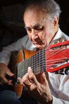 An elderly man in white shirt playing an acoustic guitar. Dark background. Focus on the hand.