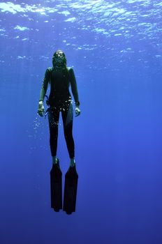 young girl with long fins rise from the deep of sea to the surface and sun