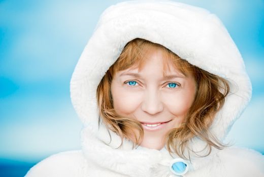 Adult woman in a white fur coat with a blue brooch against the winter sky. smiling. closeup.