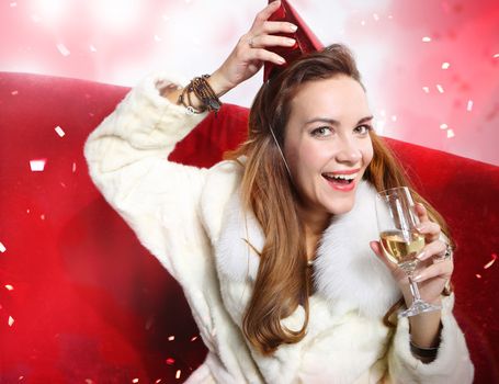 Girl with red gift and a glass of champagne sitting on a red sofa