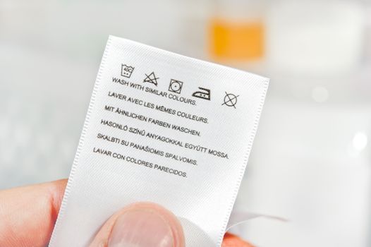 Hand holding clothes label with cleaning instructions.