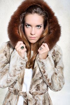 Beautiful long-haired model posing in a fur coat with unhappy expression