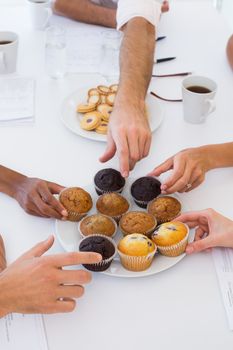 Business people taking muffins from plate in the office