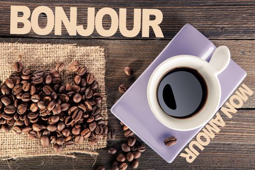 cup of black coffee with some coffee beans scattered on wooden table. point of view from below