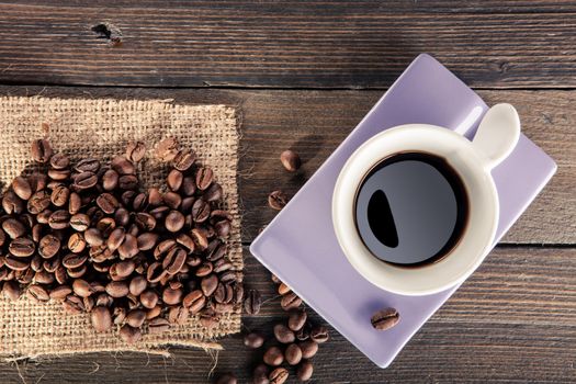 cup of black coffee with some coffee beans scattered on wooden table. point of view from below