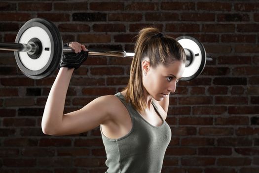 Portrait of Attractive fit woman lifting dumbbells on brick background 