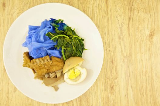 Blue rice noodle with fried tofu, spinach, abalone mushroom and egg boiled in the gravy vegetarian on wood background.