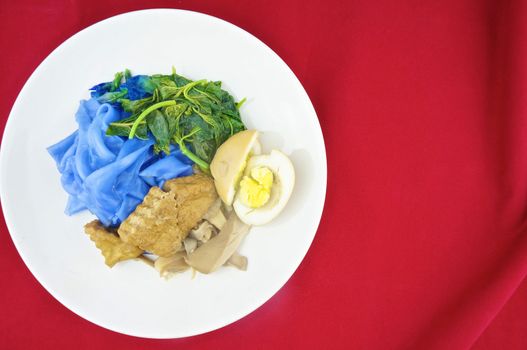 Blue rice noodle with fried tofu, spinach, abalone mushroom and egg boiled in the gravy vegetarian on red background.