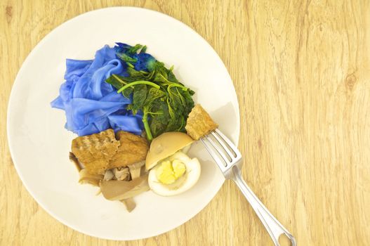 Eating blue rice noodle with fried tofu, spinach, abalone mushroom and egg boiled in the gravy by fork vegetarian on wood background.