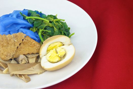 Close up blue rice noodle with fried tofu, spinach, abalone mushroom and egg boiled in the gravy vegetarian on red background.