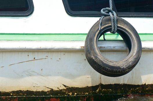 Old used tire with rope on the side of boat for fender.
