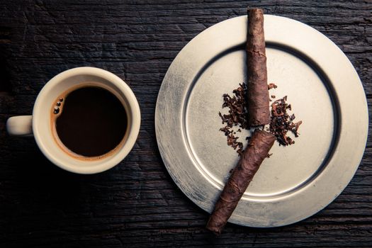 cigars in ashtray that look like the hands of a watch. they sign seven o'clock. it's time to wake up so there's a cup of coffee on the left.