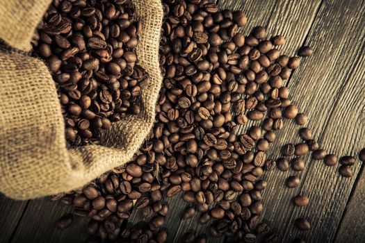 close up of jute bag full of coffee beans, and some coffee beans scattered on a wooden table