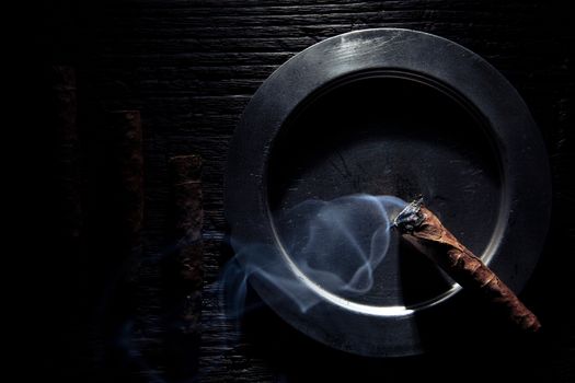 geometric composition of cigars end ashtray. the cigar is lit and it's steaming.