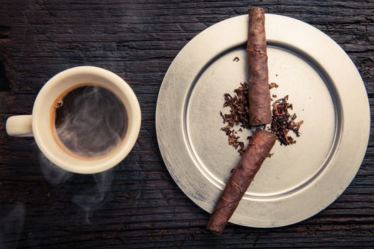 cigars in ashtray that look like the hands of a watch. they sign seven o'clock. it's time to wake up so there's a cup of steaming coffee on the left.