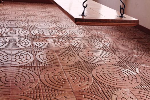Intricately designed terracota tiles in a classic design are used on a verandah which has a flat wooden swing of polished teak wood.