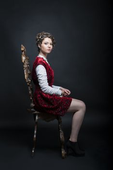 Portrait of beautiful Caucasian model in red Victorian-style velvet dress, seated on wooden chair
