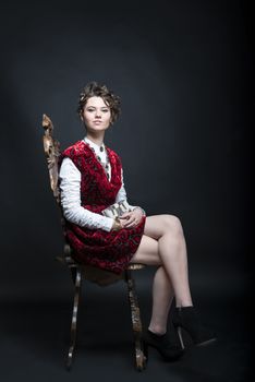 Portrait of beautiful Caucasian model in red Victorian-style velvet dress, seated on wooden chair