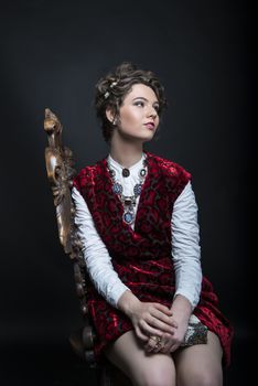 Portrait of beautiful Caucasian model in red Victorian-style velvet dress, seated on wooden chair
