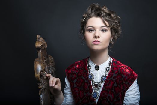 Portrait of beautiful Caucasian model in red Victorian-style velvet dress, seated on wooden chair
