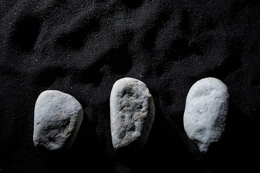 three white stones on black sand