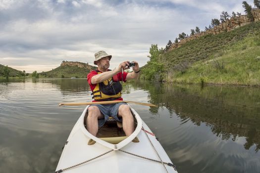 senior athletic paddler in a  decked expedition canoe photographing on a lake with green vegetation - Horsetooth Reservoir, Fort Collins, Colorado