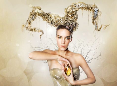woman with golden horns is holding a perfume bottle