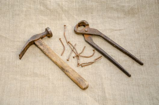 rusty hammer with nails and old pliers lying on linen texture